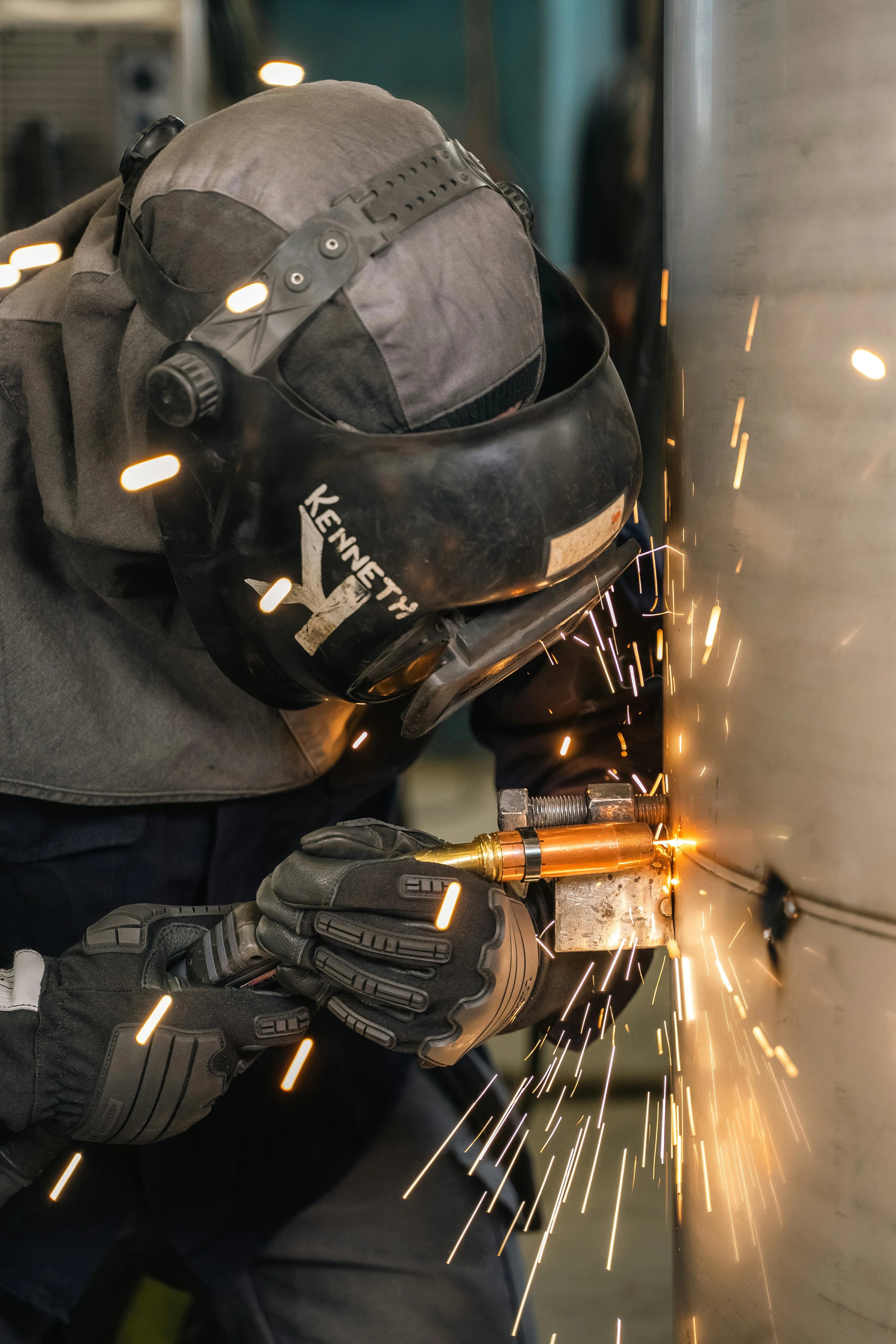 Welder in protective gear and gloves welding metal with sparks flying.