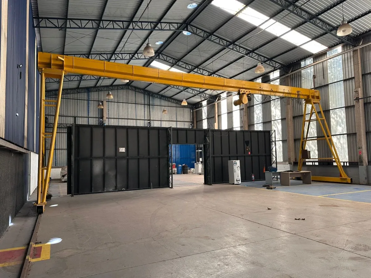 Interior of an empty industrial warehouse with a large yellow overhead crane and black metal partitions.